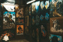 Gallery wall display of diverse, colorful wall art paintings with animal and historical themes in a dimly lit room.