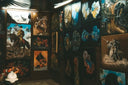 Gallery wall display of diverse, colorful wall art paintings with animal and historical themes in a dimly lit room.
