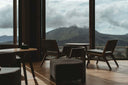 Modern lounge area with wooden chairs and ottoman overlooking mountain view through large glass windows