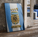 Argentina football national team crest jersey print in a black frame leaning beside a vintage door on parquet