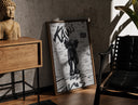 Walnut-framed KAWS Companion figure standing print leaning against a sunlit rustic brick wall