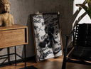 Walnut-framed Black KAWS Companion figure sitting print leaning against a sunlit rustic brick wall