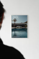 Car art in white frame on wall — Porsche 911 poolside scene with silhouetted person visible in foreground
