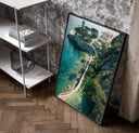 Cliffside coastal luxury villa estate poster in a black frame leaning beside a shelf in a raw-plaster loft