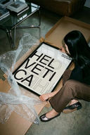 Woman lifting a Helvetica Typography Swiss Design wall art poster out of brown cardboard shipping tube