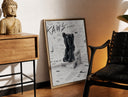 Brass-framed KAWS Companion figure sitting print leaning in a warm styled corner by a sculpture