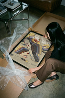 Woman unpacking framed Nike Air Max 97 Sean Wotherspoon poster showing colorful striped sneaker artwork from cardboard box