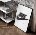 Blurred Nike swoosh logo poster in a black frame leaning beside a shelf in a raw-plaster loft