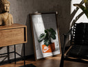 Walnut-framed Monstera plant in Nike shoe box print leaning against a sunlit rustic brick wall