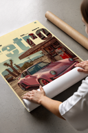 Person unrolling a Porsche 911 Retro Gas Station art print with vintage gas station on a smooth concrete floor