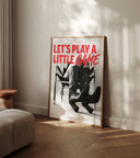 Unframed Let's Play a Little Game poster leaning against cream wall in warm styled room with wooden herringbone floor and round wooden side table