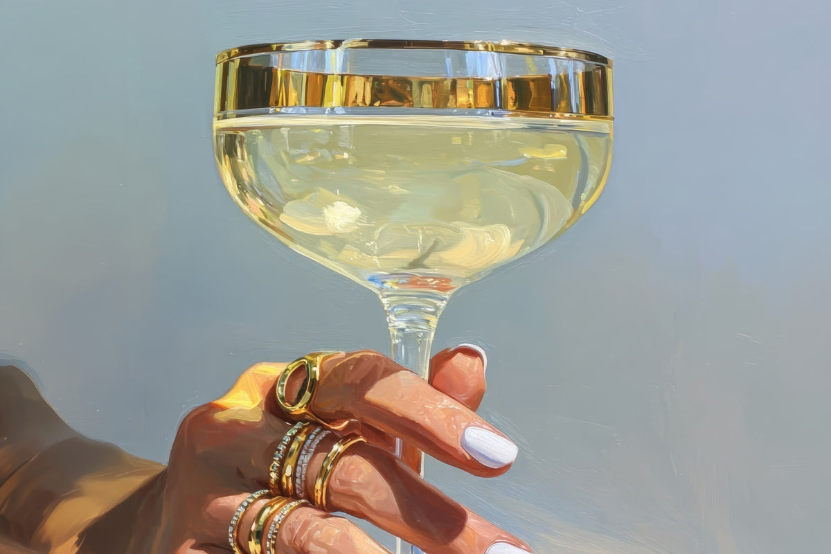 Golden Coupe on Blue cocktail print: a hand with gold rings holding a gold-rimmed champagne coupe against a pale blue background