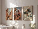 Three standard size posters with beach and fashion themes displayed in wooden frames on a sunlit wall above a white sideboard.