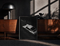 Black-framed Silver Porsche 911 parked in alley print on a moody console with designer coffee-table books