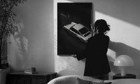 Silver Porsche 911 parked in alley print in a slim black frame being hung on a sunlit wall in a monochrome room