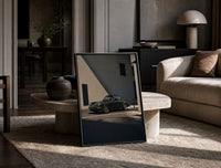 Vintage green Porsche 911 coupe print in a black frame leaning on a travertine table in a sunlit lounge