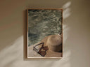 Close look at vintage accessories including a sunhat and sunglasses beside shimmering water, for sophisticated decor.