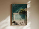 Aerial view of a tennis court surrounded by water and greenery framed as wall art in a minimalist room