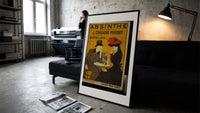 Man and woman drinking absinthe at table print in a slim black frame leaning on a dark sofa in a concrete print studio