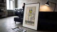 Ace of Cups tarot card print in a slim black frame leaning on a dark sofa in a concrete print studio