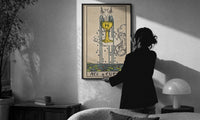 Ace of Cups print in a slim black frame being hung on a sunlit wall in a monochrome room