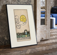 Hand holding pentacle coin print in a black frame leaning beside a vintage door on parquet