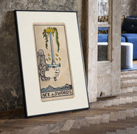 Hand holding upright sword with crown print in a black frame leaning beside a vintage door on parquet