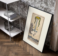 Hand holding upright sword with crown poster in a black frame leaning beside a shelf in a raw-plaster loft