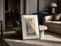 Hand holding upright sword with crown print in a black frame leaning on a travertine table in a sunlit lounge