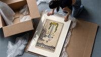 Hand holding upright sword with crown framed print being unpacked from protective bubble wrap and a box