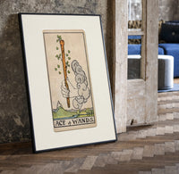 Hand holding sprouting wooden wand print in a black frame leaning beside a vintage door on parquet