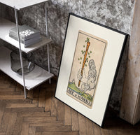 Hand holding sprouting wooden wand poster in a black frame leaning beside a shelf in a raw-plaster loft