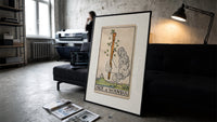 Hand holding sprouting wooden wand print in a slim black frame leaning on a dark sofa in a concrete print studio