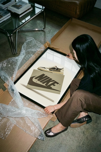 A white poster featuring the Air Jordan 1 Travis Scott Mocha Sneaker above a tan Nike logo sits partially rolled.