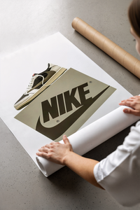 White poster of the Air Jordan 1 Travis Scott Mocha sneaker above a tan Nike logo sitting partially rolled