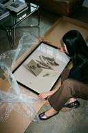 Woman unboxing framed Air Jordan 1 Travis Scott Reverse Mocha artwork from cardboard packaging on concrete floor