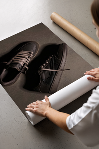 Woman unrolling poster print of Air Jordan 1 Travis Scott Velvet Brown Dark Mocha sneakers on concrete floor