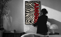Amore Zebra Print in a slim black frame being hung on a sunlit wall in a monochrome room