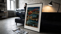 Antibes coastal town scene print in a slim black frame leaning on a dark sofa in a concrete print studio