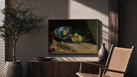 Apples and lemon in blue bowl print in a wood frame above a fluted sideboard beside an olive tree