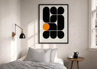 Arches Composition print in a black frame above a bed with striped linens, a brass wall lamp and a sunlit window