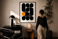 Arches Composition print in a black frame on a sunlit plaster wall, a woman looking on beside a mushroom lamp