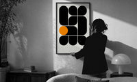 Arches Composition print in a slim black frame being hung on a sunlit wall in a monochrome room