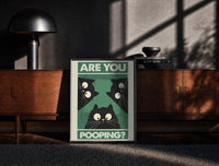 Black-framed Are You Pooping Three Cats print on the floor in front of a dark wooden console