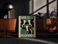 Black-framed Are You Pooping Three Cows print on the floor in front of a dark wooden console
