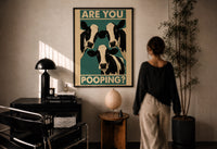Are You Pooping Three Cows print in a black frame on a sunlit plaster wall, a woman looking on beside a mushroom lamp