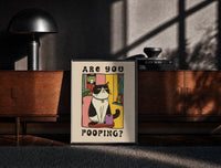Black-framed Are You Pooping Tuxedo Cat print on the floor in front of a dark wooden console