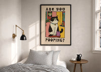 Are You Pooping Tuxedo Cat print in a black frame above a bed with striped linens, a brass wall lamp and a sunlit window