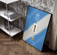FIFA World Cup 2026 Argentina logo poster in a black frame leaning beside a shelf in a raw-plaster loft