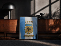 Black-framed Argentina football national team crest jersey print on a moody console with designer coffee-table books